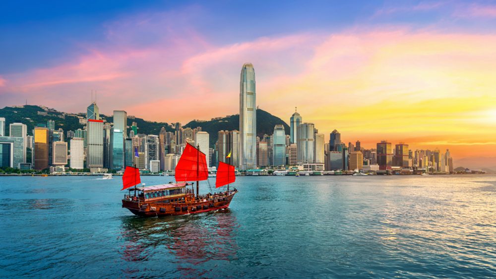 Traditional red-sailed junk boat on Victoria Harbour with the Hong Kong skyline at sunset